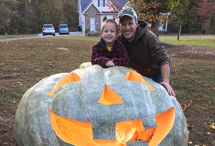 Elijah Meck and his son Owen pose with their prizewinning pumpkin turned jack-o'-lantern.