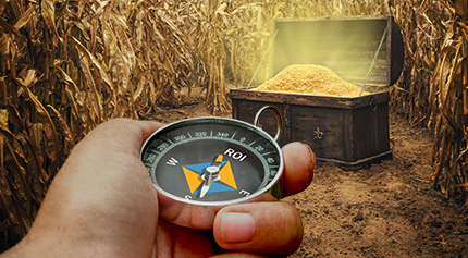 A hand holding a compass in front of a treasure chest.
